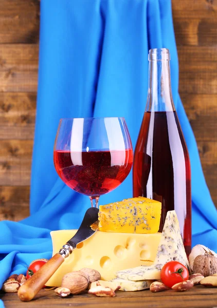 Pink wine and different kinds of cheese on wooden background — Stock Photo, Image