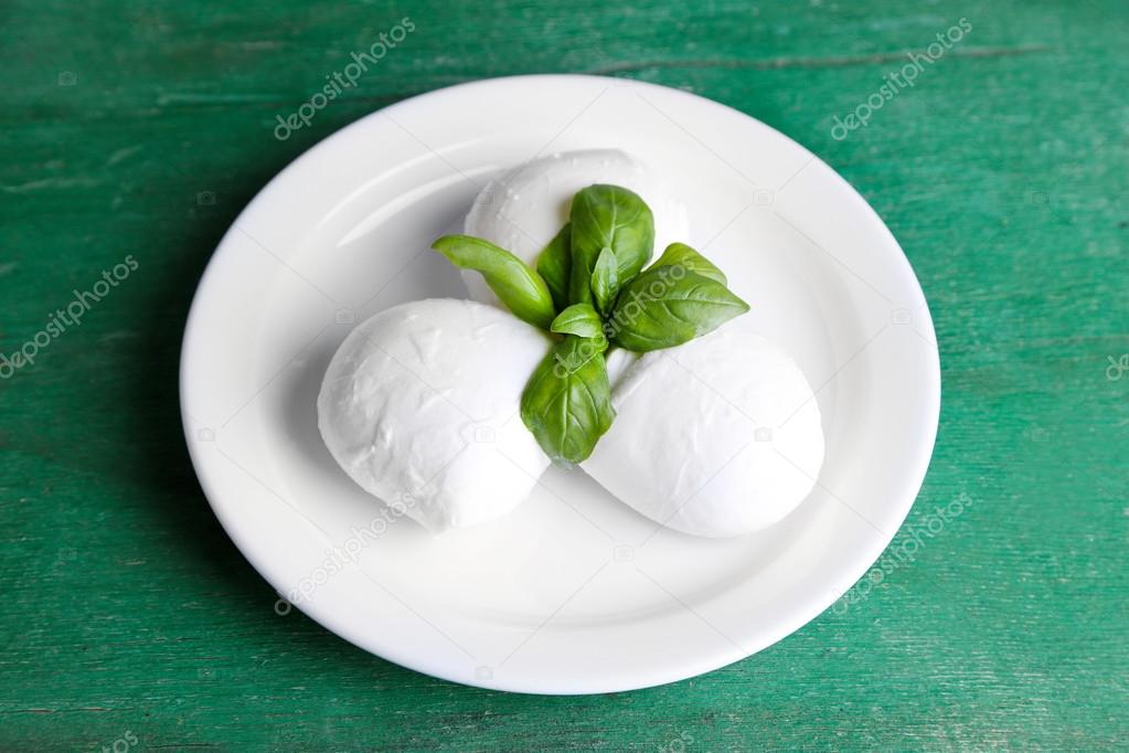 Tasty mozzarella cheese with basil on plate  on wooden background