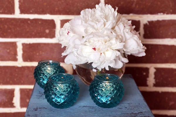 Glass candlesticks and flowers on stand, on bricks background — Stock Photo, Image