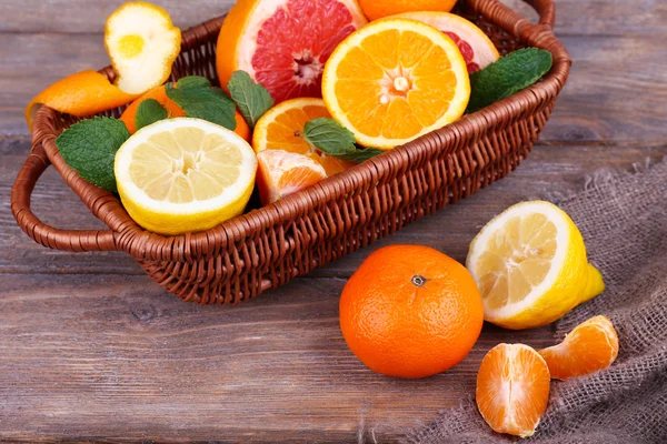 Čerstvé citrusové plody se zelenými listy v proutěném koši na dřevěný stůl pozadí — Stock fotografie