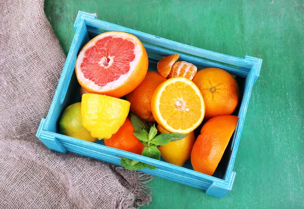Verse citrusvruchten met groene bladeren in houten doos op houten achtergrond — Stockfoto