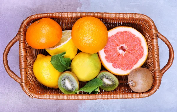 Frutas exóticas frescas con hojas verdes en canasta de mimbre sobre fondo de madera — Foto de Stock