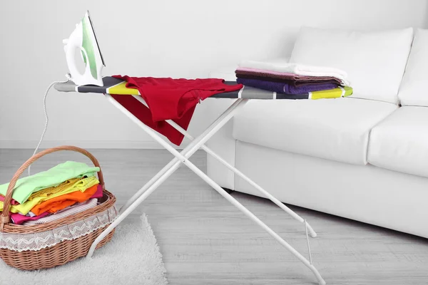 Basket with laundry and ironing board on light background — Stock Photo, Image