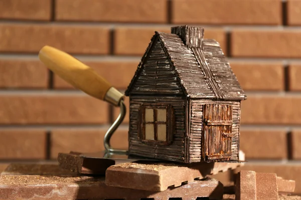 Деревянный игрушечный домик на лопатке и плитка на фоне кирпичной стены — стоковое фото