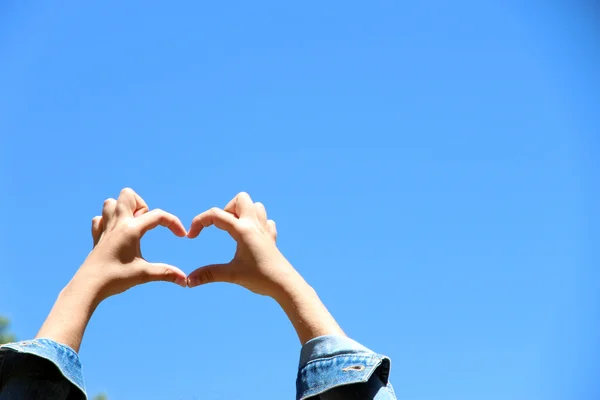 Jeune fille tenant la main en forme de coeur encadrant sur fond bleu ciel — Photo