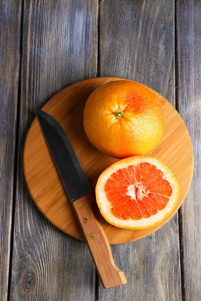 Ripe grapefruits and knife on cutting board, on wooden background — Stock Photo, Image