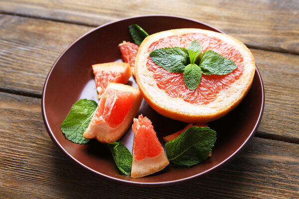 Ripe chopped grapefruit with mint leaves on plate, on wooden background