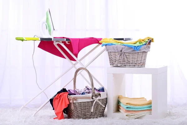 Baskets with laundry and ironing board on light home interior background — Stock Photo, Image