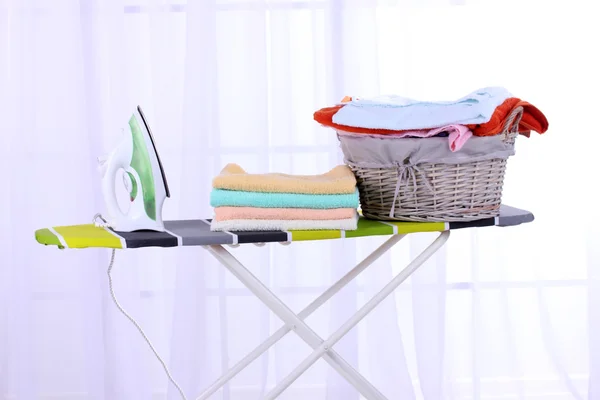 Basket with laundry and ironing board on light home interior background — Stock Photo, Image