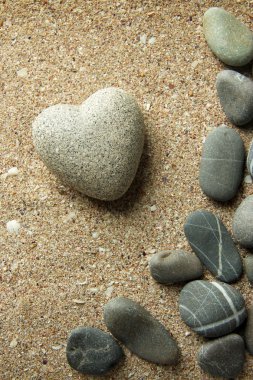 Grey stone in shape of heart, on sand background clipart