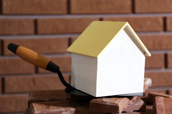 Wooden toy house on trowel and tiles on brick wall background — Stock Photo, Image