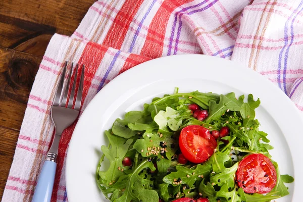 Зеленый салат из рукколы, помидоров и кунжута на тарелке, на деревянном фоне — стоковое фото