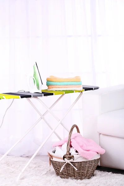 Baskets with laundry and ironing board on light home interior background — Stock Photo, Image