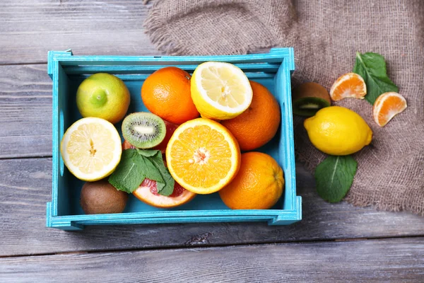 Fruits exotiques frais avec des feuilles vertes dans une boîte en bois sur fond en bois de couleur — Photo