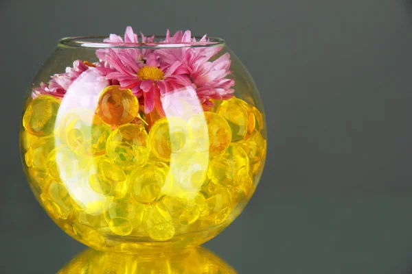 Hermosas flores en jarrón con hidrogel en la mesa sobre fondo gris —  Fotos de Stock