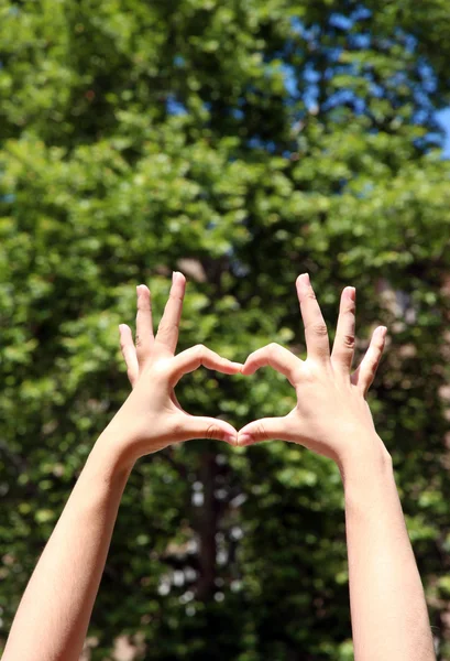 Young girl holding hands in heart shape framing on nature background — Stock Photo, Image