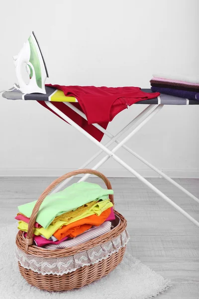 Basket with laundry and ironing board on light background — Stock Photo, Image