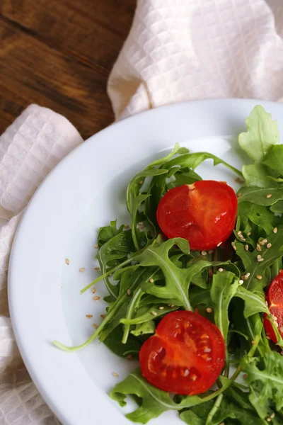 Groene salade gemaakt met rucola, tomaten en sesam op plaat, op houten achtergrond — Stockfoto