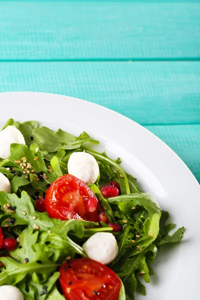 Green salad made with  arugula, tomatoes, cheese mozzarella balls and sesame  on plate, on color wooden background — Stock Photo, Image