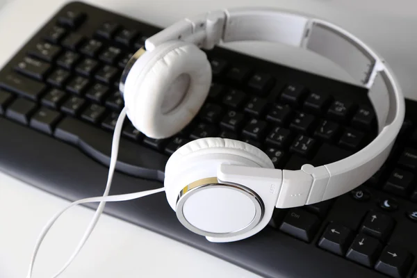 Sluchátka a klávesnice close-up na pozadí bílý stůl — Stock fotografie