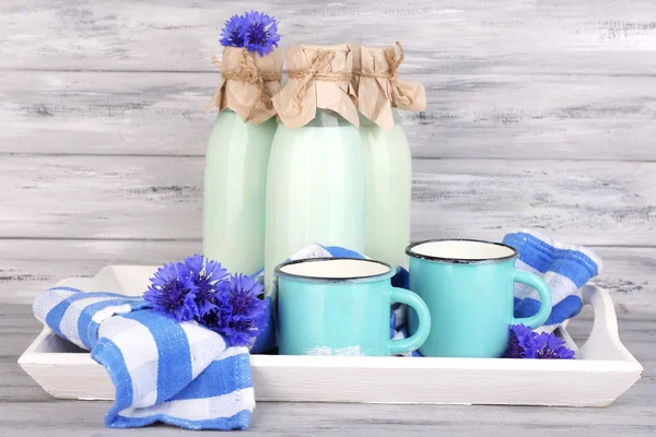 Bottles and cups of milk with cornflowers on wooden tray — Stock Photo, Image