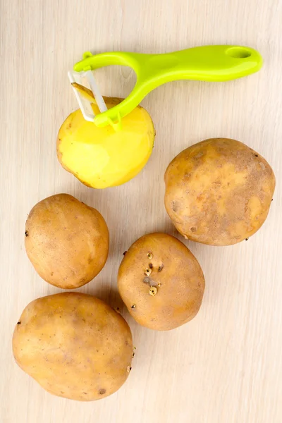 Pelapatate e patate sul tavolo di legno — Foto Stock
