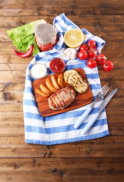 Gegrilde biefstuk, gegrilde groenten en gebakken aardappel stukken op houten plank op tabelachtergrond — Stockfoto