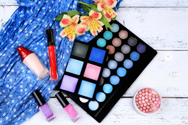 Eyeshadow, brush, lipstick and flowers on color wooden background — Stock Photo, Image