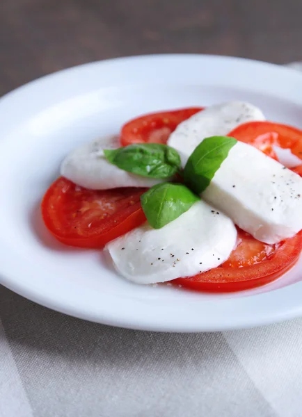 Caprese salad with mozarella cheese, tomatoes and basil on plate, on wooden table background — Stock Photo, Image