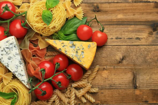 Různé těstoviny, sýra a rajčat na dřevěný stůl detail — Stock fotografie