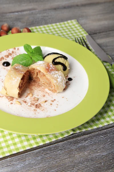 Tasty homemade apple strudel with nuts, mint leaves and ice-cream on plate, on wooden background — Stock Photo, Image