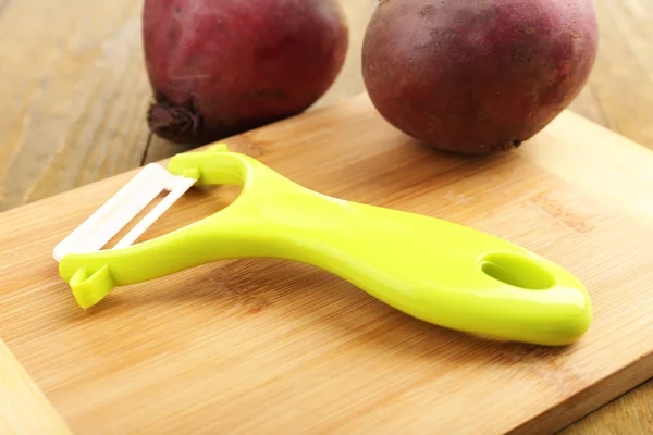 Peeler and beet on wooden table — Stock Photo, Image