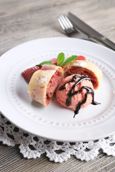 Leckerer hausgemachter Strudel mit Eis, frischen Erdbeer- und Minzblättern auf Teller, auf Holzgrund — Stockfoto