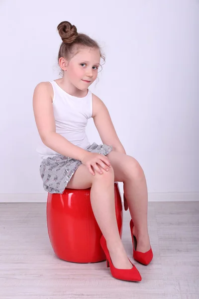 Beautiful small girl in big shoes sitting on leather ottoman