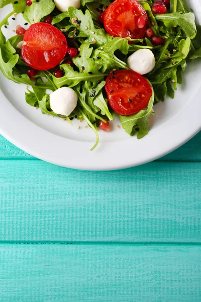 Zelený salát s rukolou, rajčaty, sýr mozzarella koule a sezam na desku, na barevné dřevěné pozadí — Stock fotografie