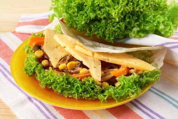 Veggie wrap filled with cheese and fresh vegetables on table, close up