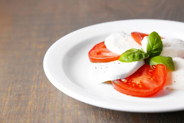 Caprese salad with mozarella cheese, tomatoes and basil on plates, on wooden table background — Stock Photo, Image