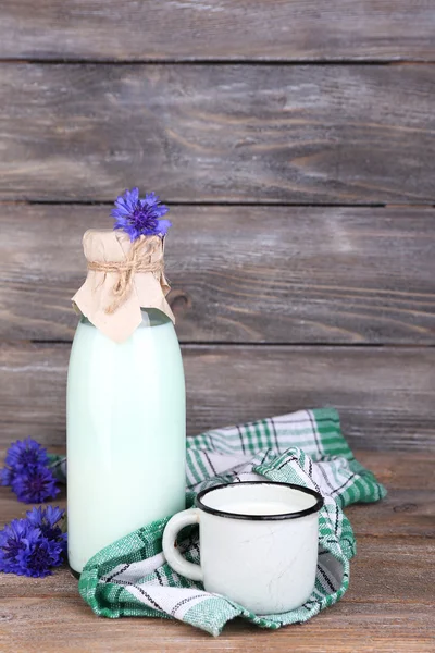 Bottle and cup of milk with cornflowers on wooden background — Stock Photo, Image