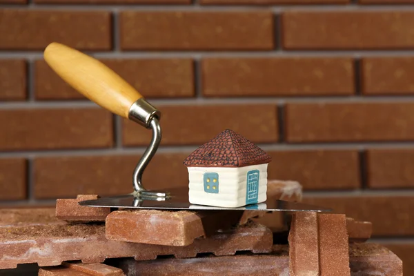 Wooden toy house on trowel and tiles on brick wall background — Stock Photo, Image