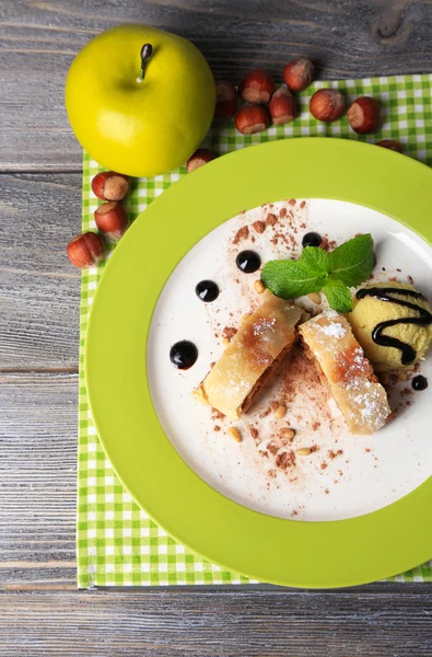 Tasty homemade apple strudel with nuts, mint leaves and ice-cream on plate, on wooden background — Stock Photo, Image