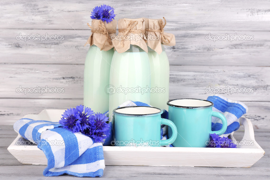 Bottles and cups of milk with cornflowers on wooden tray