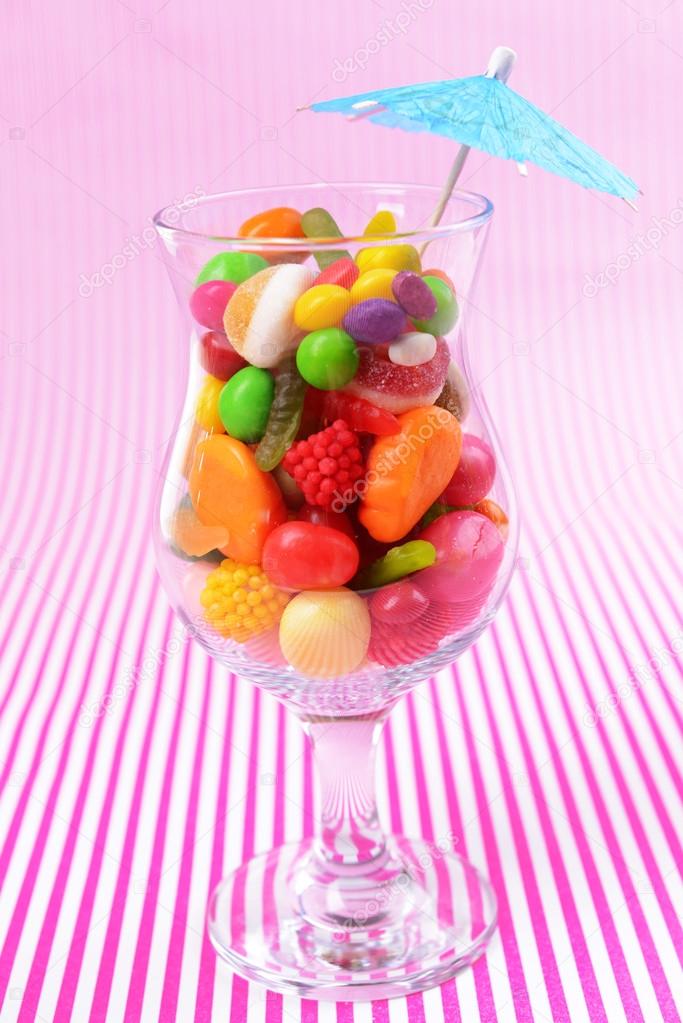 Different colorful fruit candy in glass on pink background