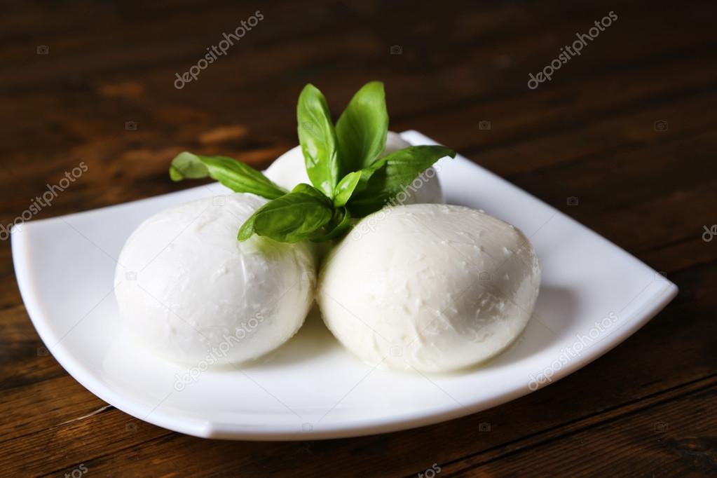 Tasty mozzarella cheese with basil on plate  on wooden background