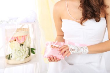 наречену в білому платті і рукавички, проведення декоративні подушки з Весільні кільця, великим планом на світлому фоні