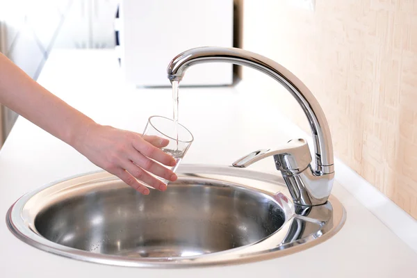 Tangan memegang gelas air dituangkan dari keran dapur — Stok Foto