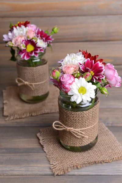 Piękny bukiet kwiatów jasny w słoiki na stole na szarym tle — Zdjęcie stockowe