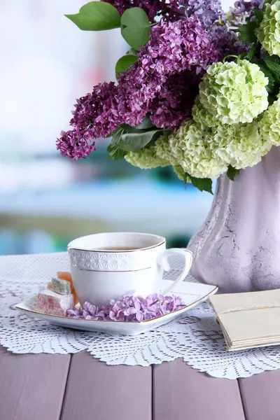 Composición con taza de té, letras viejas y hermosas flores de primavera en jarrón, sobre mesa de madera, sobre fondo brillante — Foto de Stock