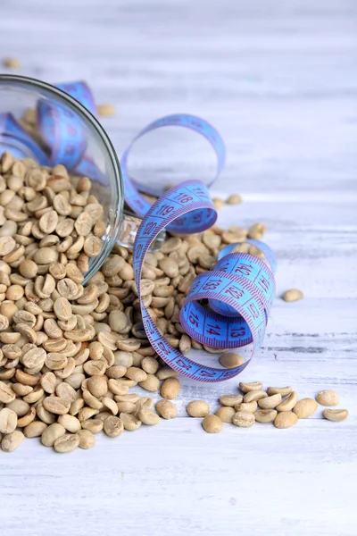 Raw green coffee beans and measuring tape, on color wooden background. Concept of weight loss — Stock Photo, Image