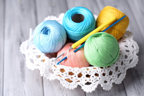 Colorful clews, napkin and crochet hook in wicker basket, on wooden background