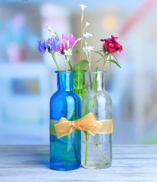 鲜艳的野花，装在瓶子里的木桌前，在明亮的背景上 — 图库照片